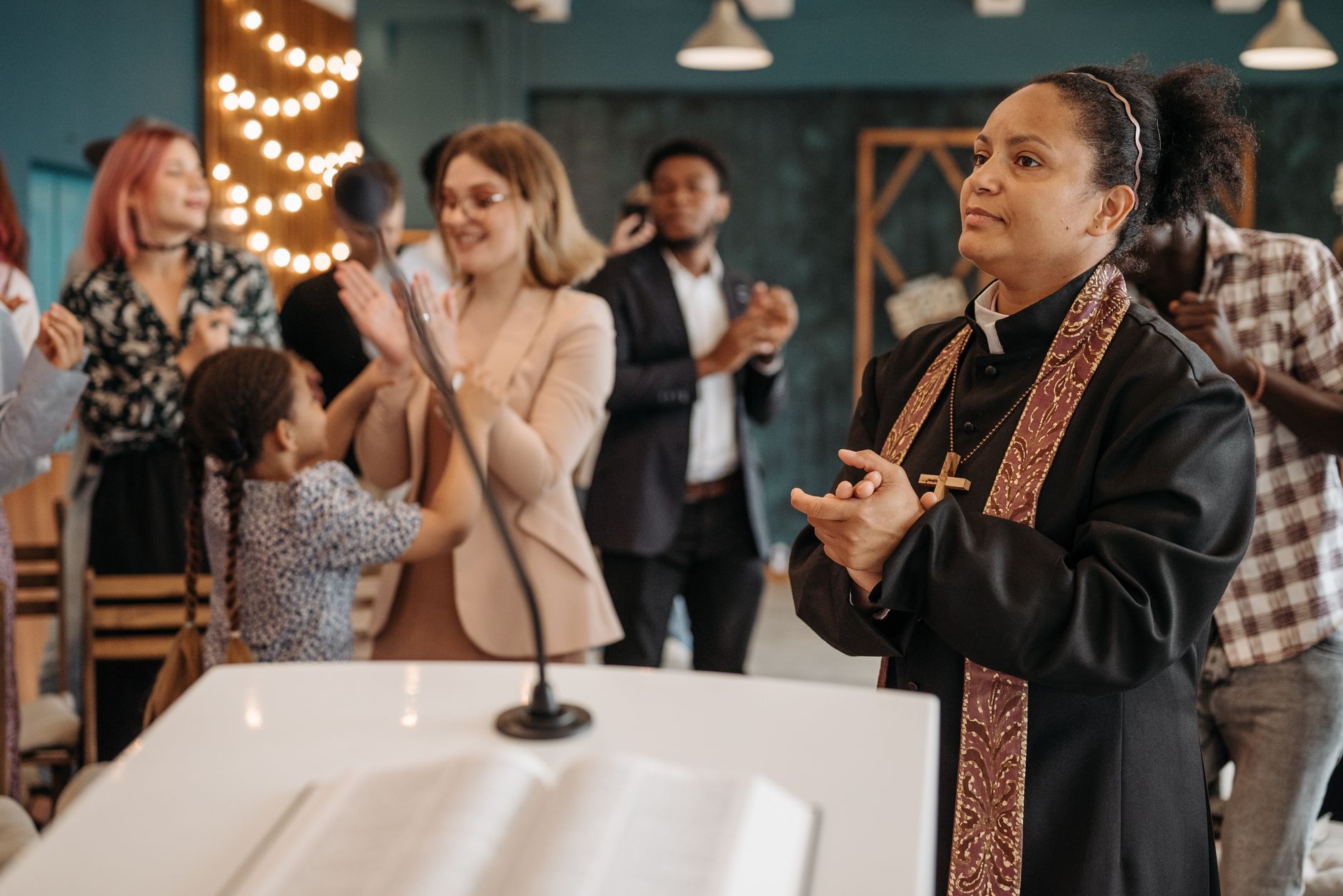 A diverse congregation clapping during a church ceremony led by a female pastor.