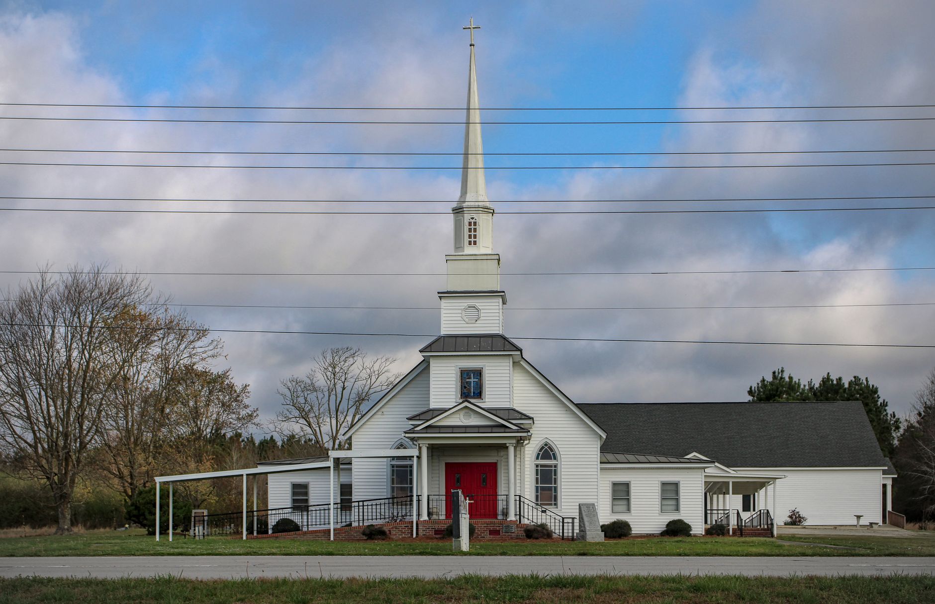 A classic white church with a red door and tall steeple under a blue sky, symbolizing spirituality and tradition.