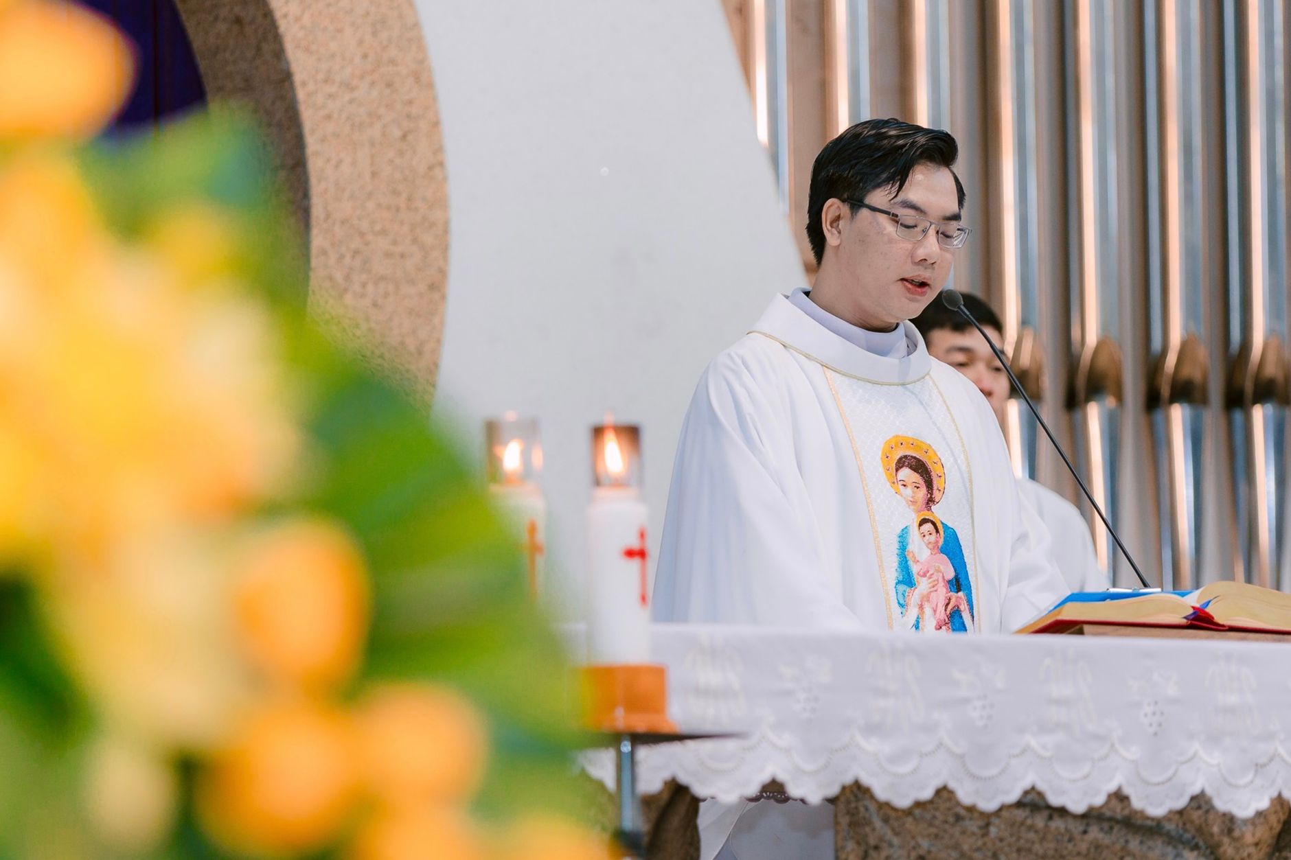 Priest delivering a sermon beside candles and religious icons inside a church.