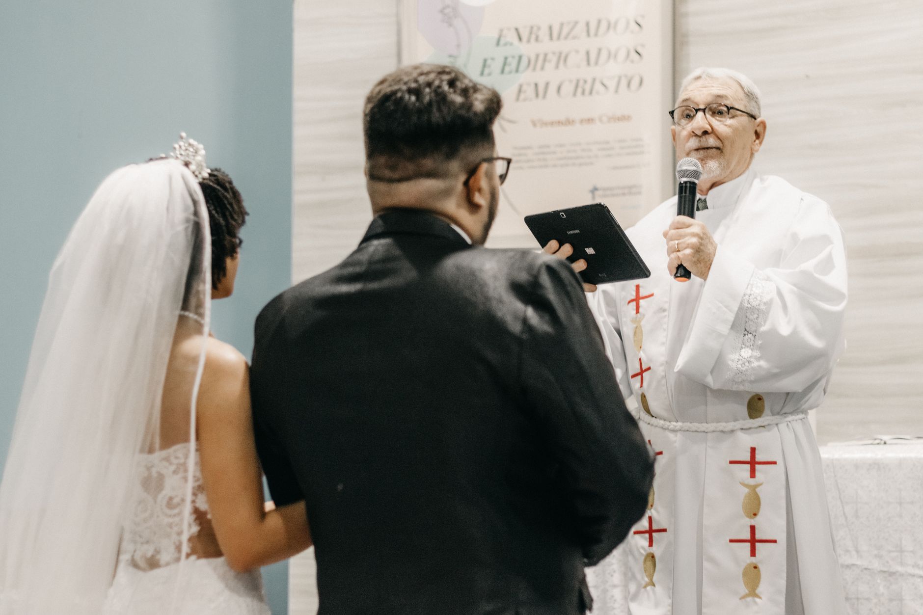 A priest officiates a wedding ceremony, speaking to the newlywed couple in a church setting.