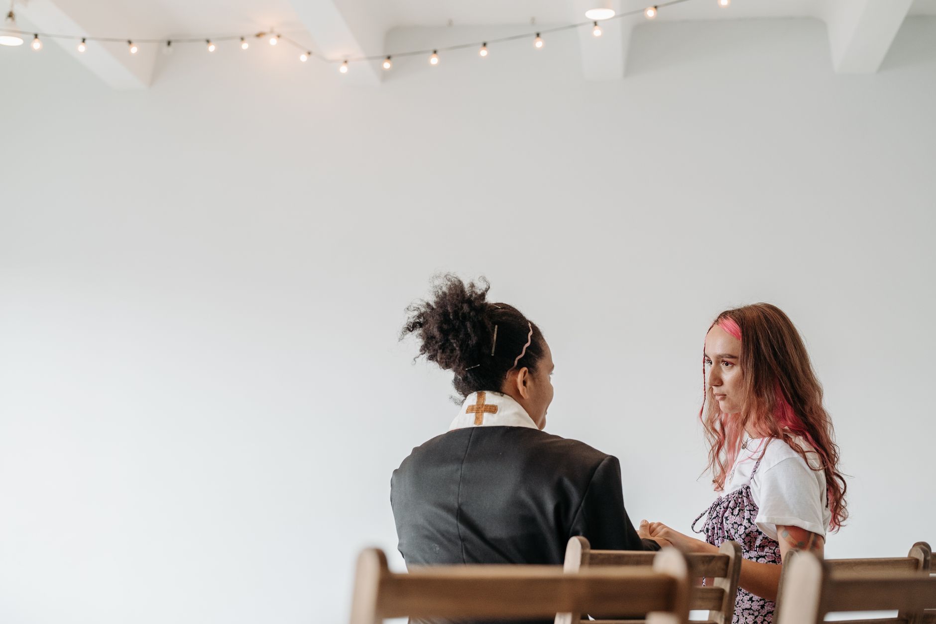 A woman pastor in a robe converses with another woman in a serene setting.