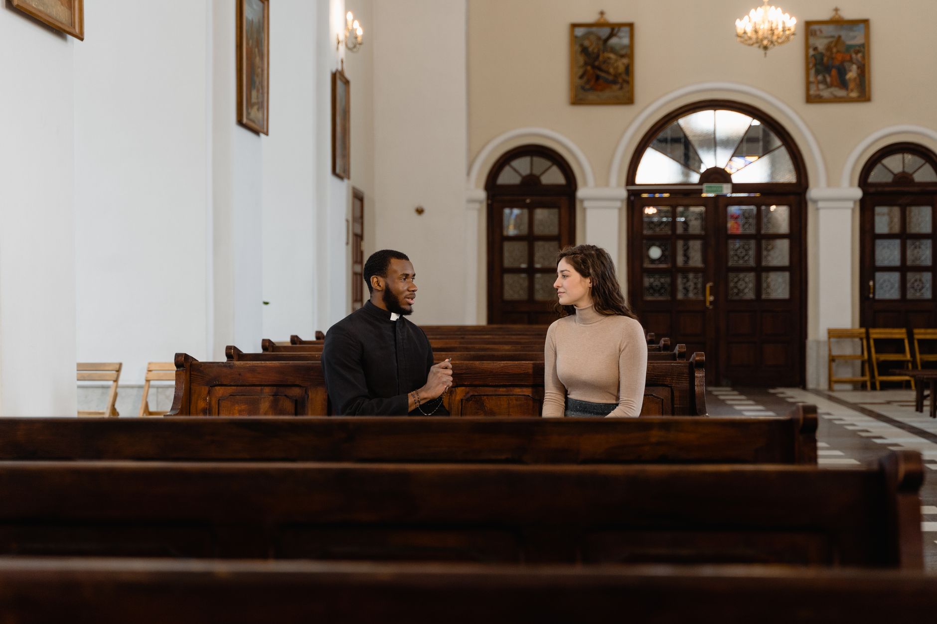A priest and a woman having a meaningful conversation in a church pew, emphasizing faith and connection.