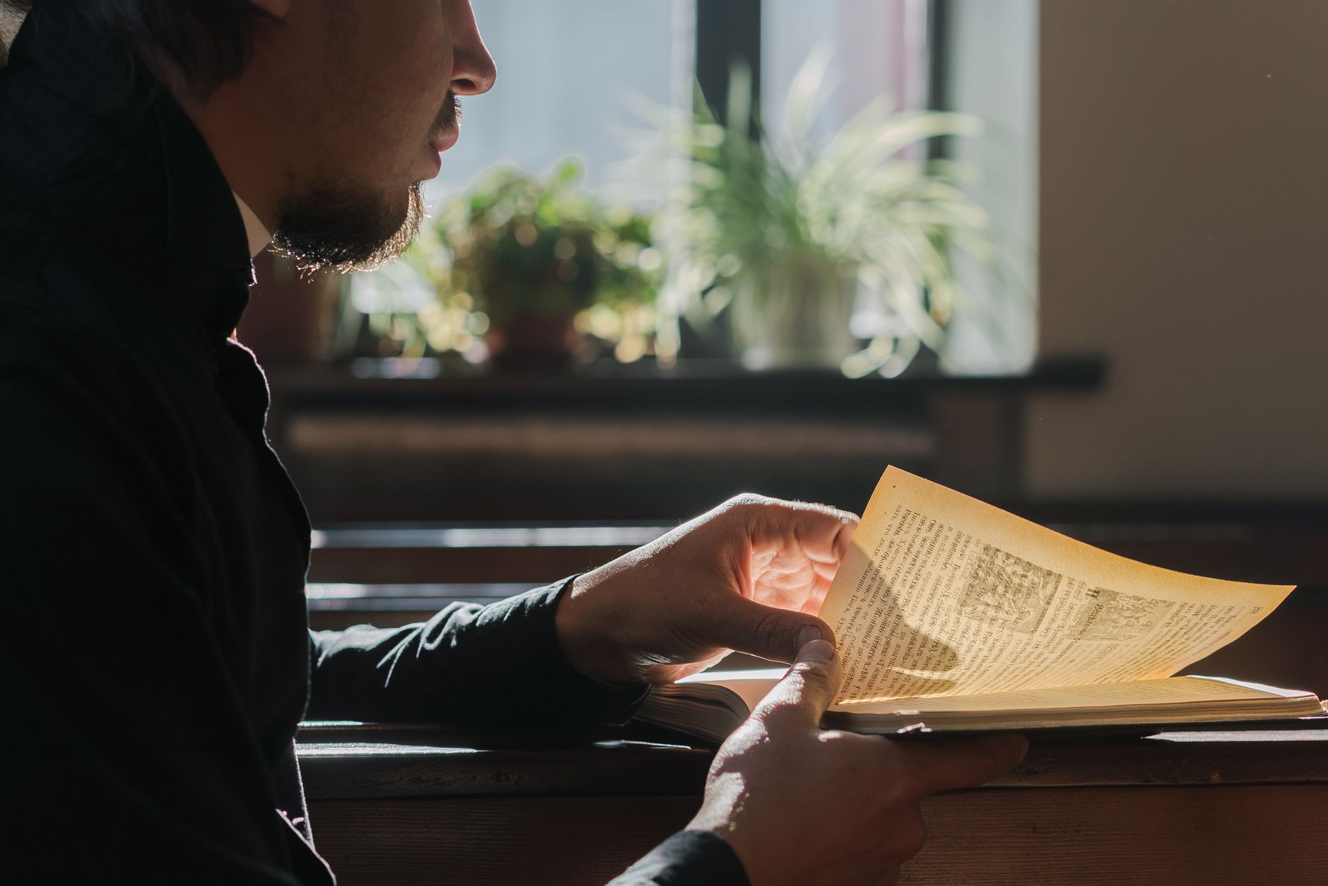 A man in black reads in a church, illuminated by window light, evoking spirituality and tranquility.