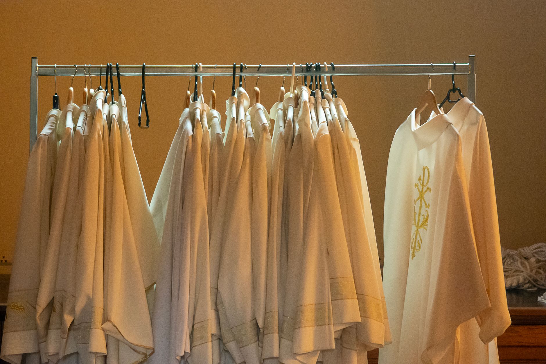 Row of white liturgical robes hanging in a church interior, bathed in soft lighting.