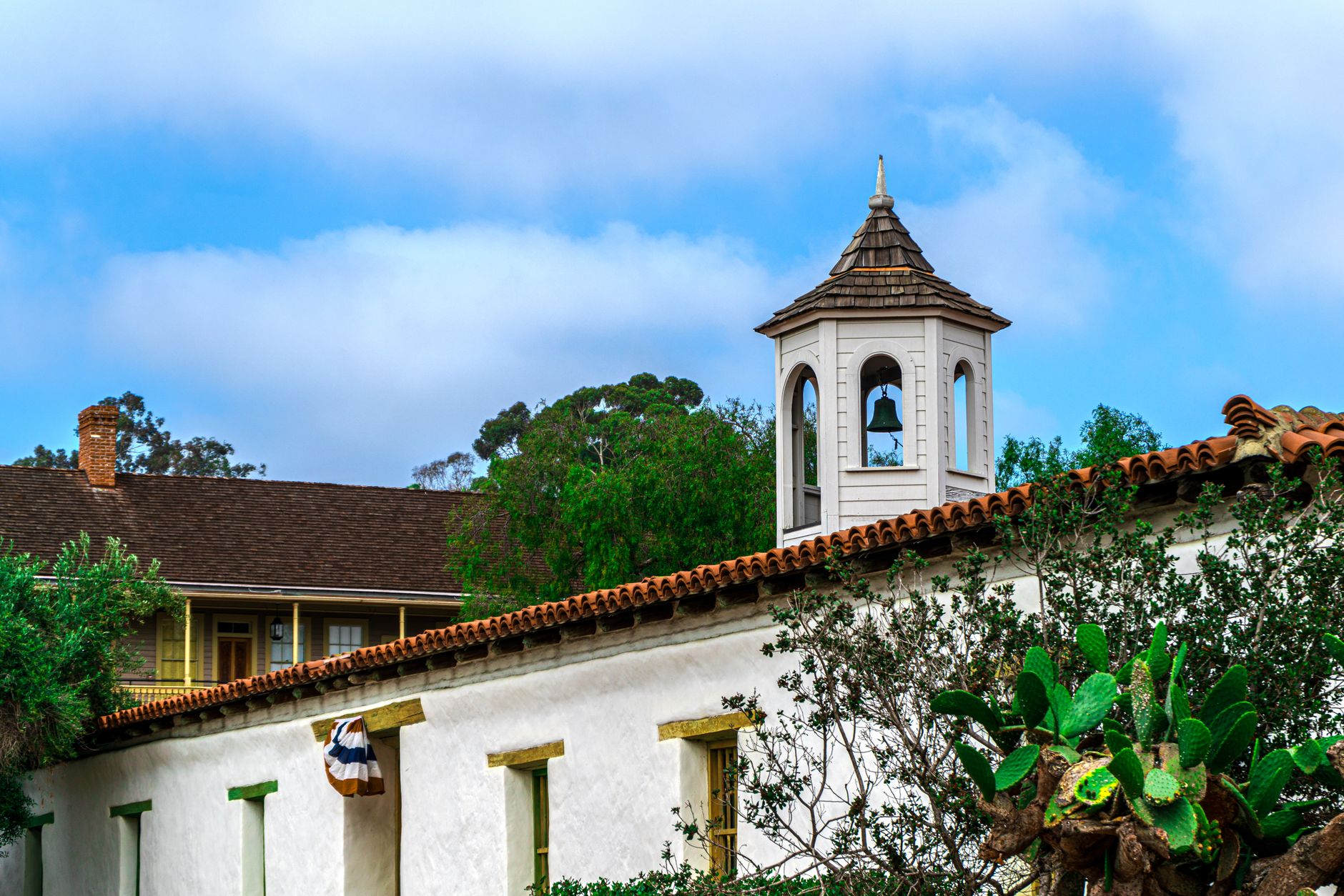 A picturesque view of a historic mission bell tower surrounded by lush greenery in San Diego, CA.