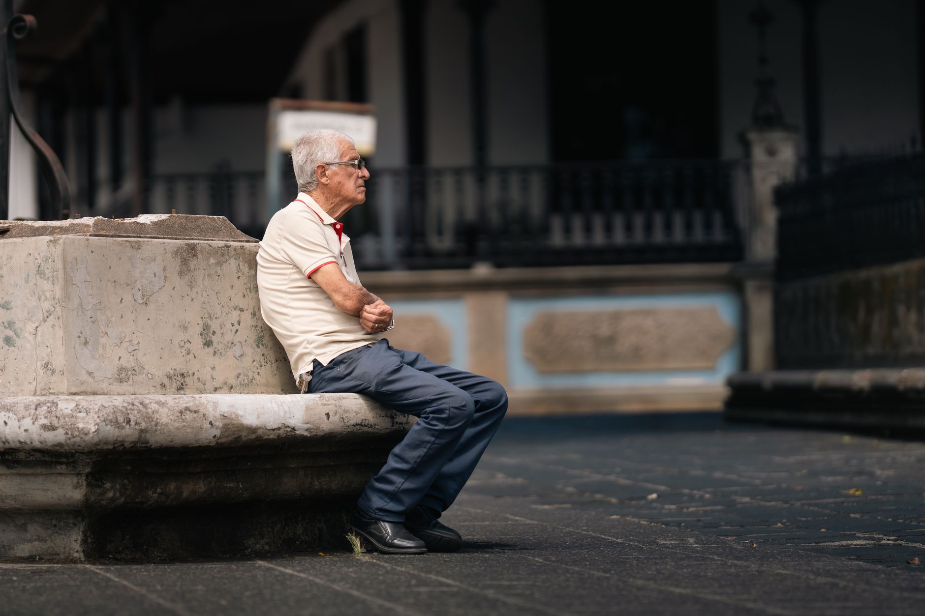A senior adult sitting contemplatively on a stone bench in San José, Costa Rica.