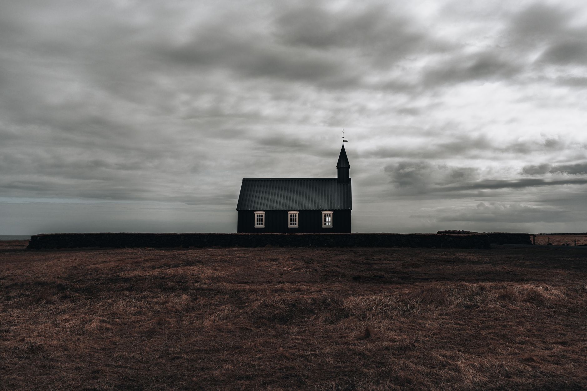 Minimalist view of a solitary church set against a moody sky, surrounded by rural fields.