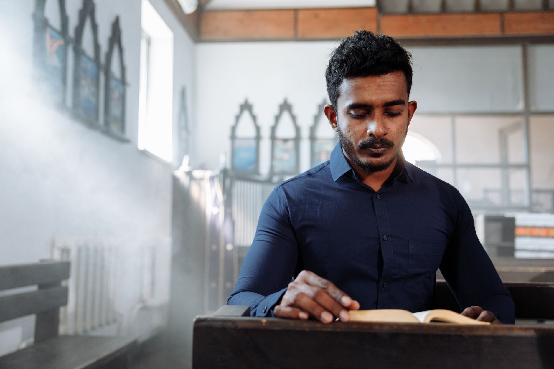 A man in a blue shirt reads a book in a sunlit church, creating a serene atmosphere.