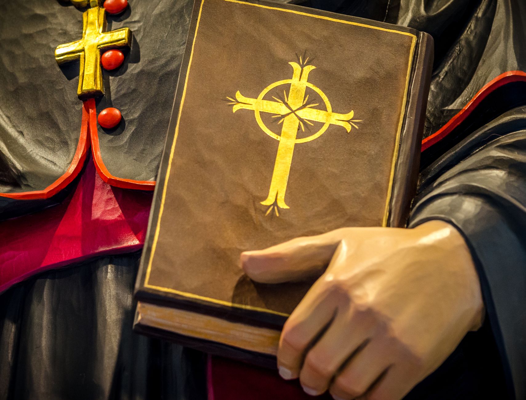 A close-up of a religious book with a cross held by a statue, symbolizing faith and spirituality.
