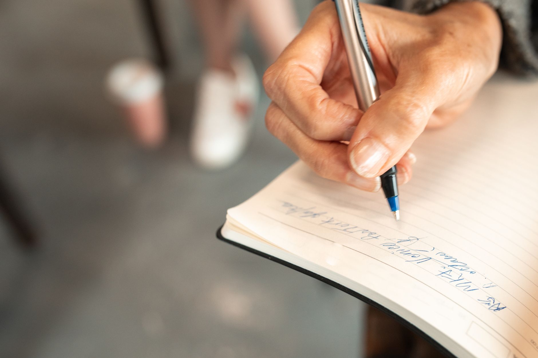 Close-up of an adult's hand writing notes in a notebook with a pen.