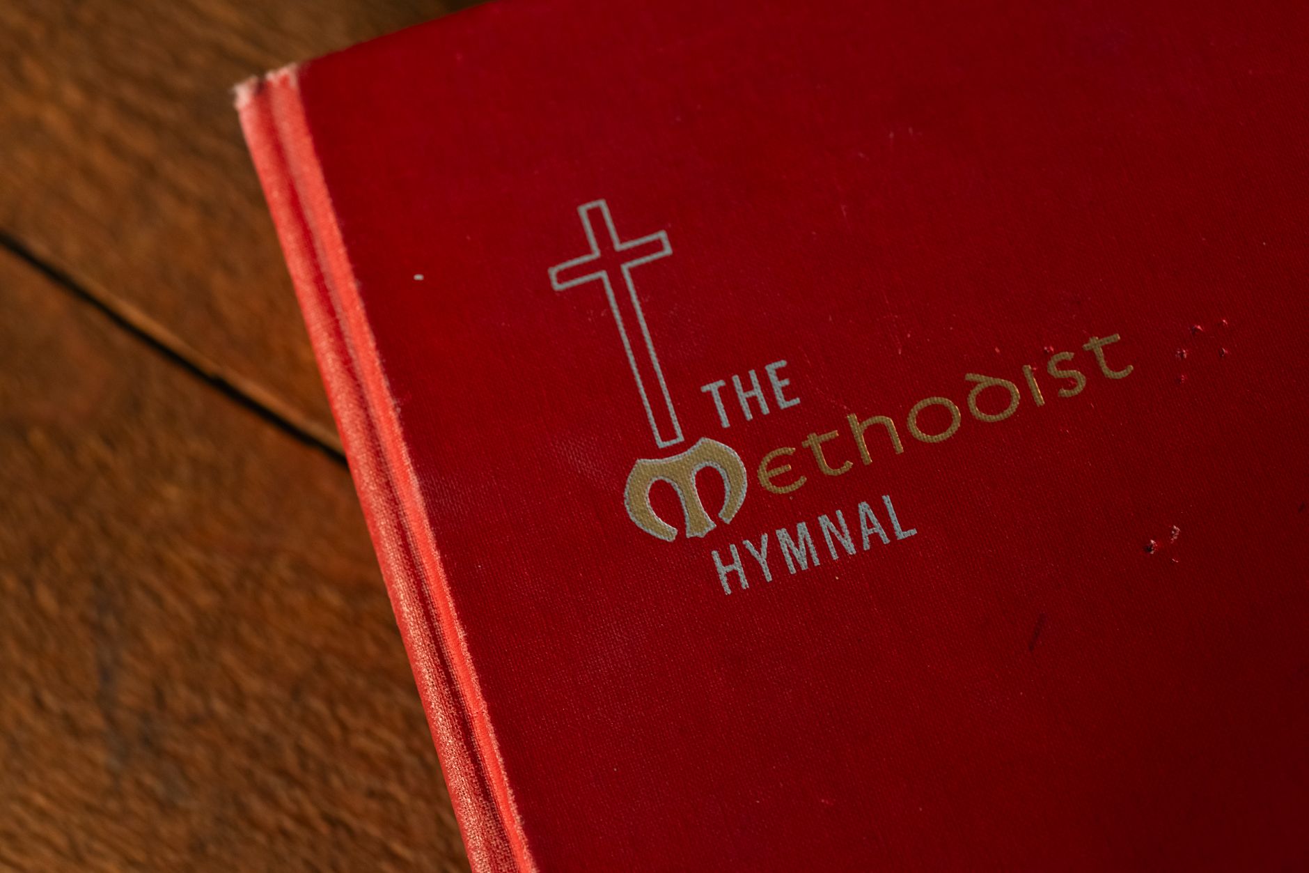 A red Methodist hymnal book with a cross symbol on a wooden table.