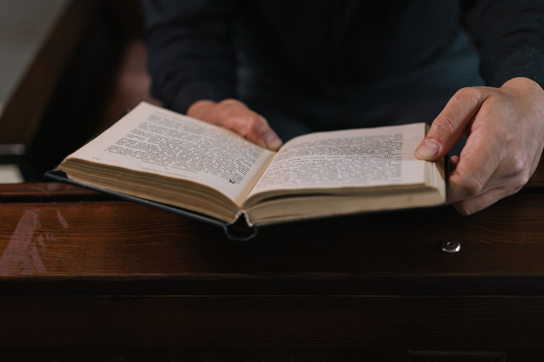 Close-up of hands holding an open book in a religious setting, perfect for themes of spirituality and contemplation.
