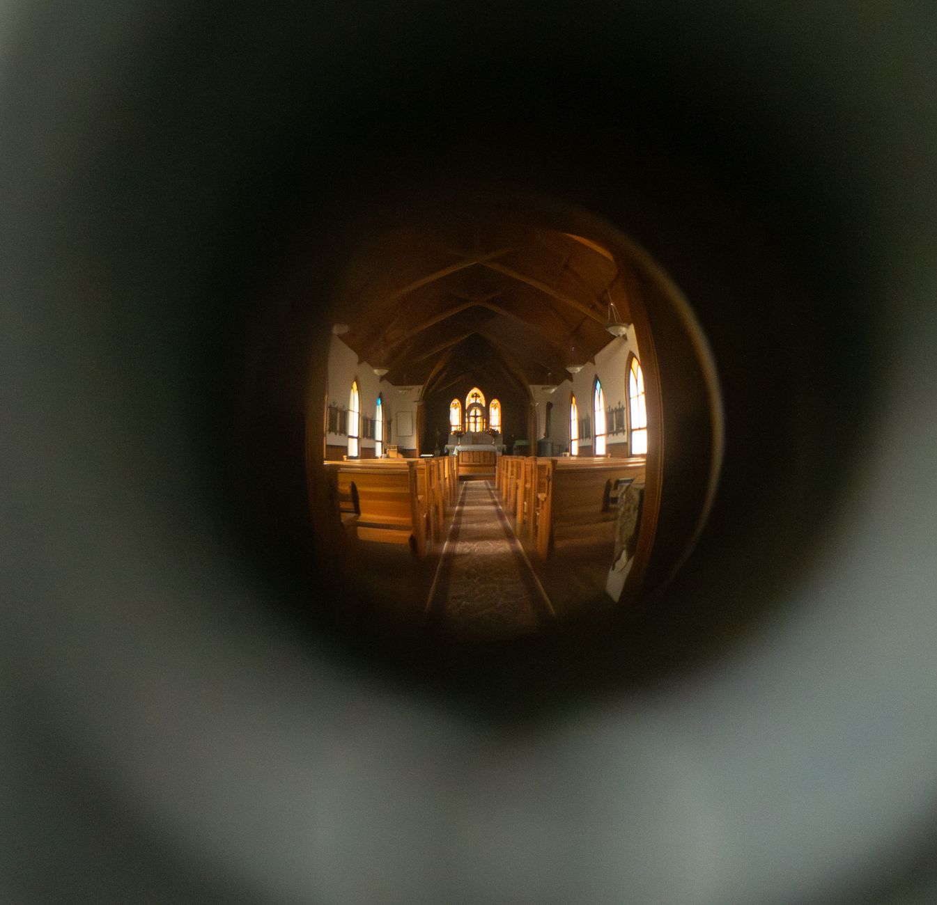 A unique keyhole perspective of a historic church interior in Silver City, Idaho, with wooden pews and stained glass windows.
