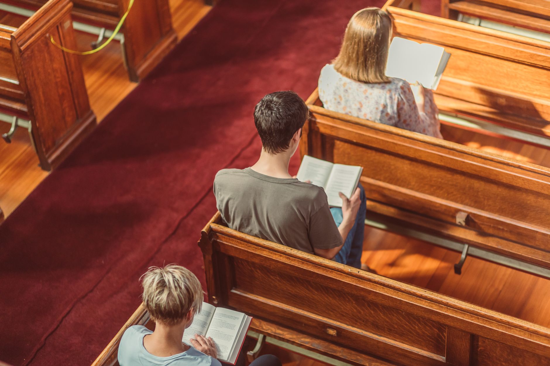 Three individuals reading books seated in a church pew, captured from above.