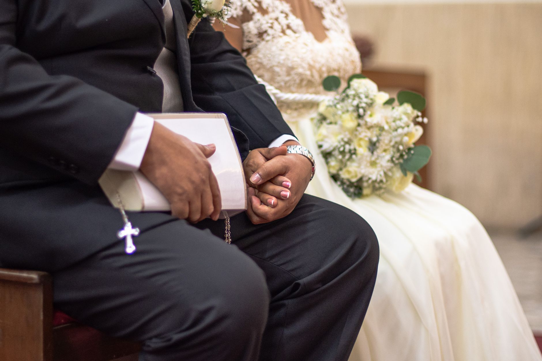 A close-up shot of a bride and groom holding hands during their wedding ceremony indoors.