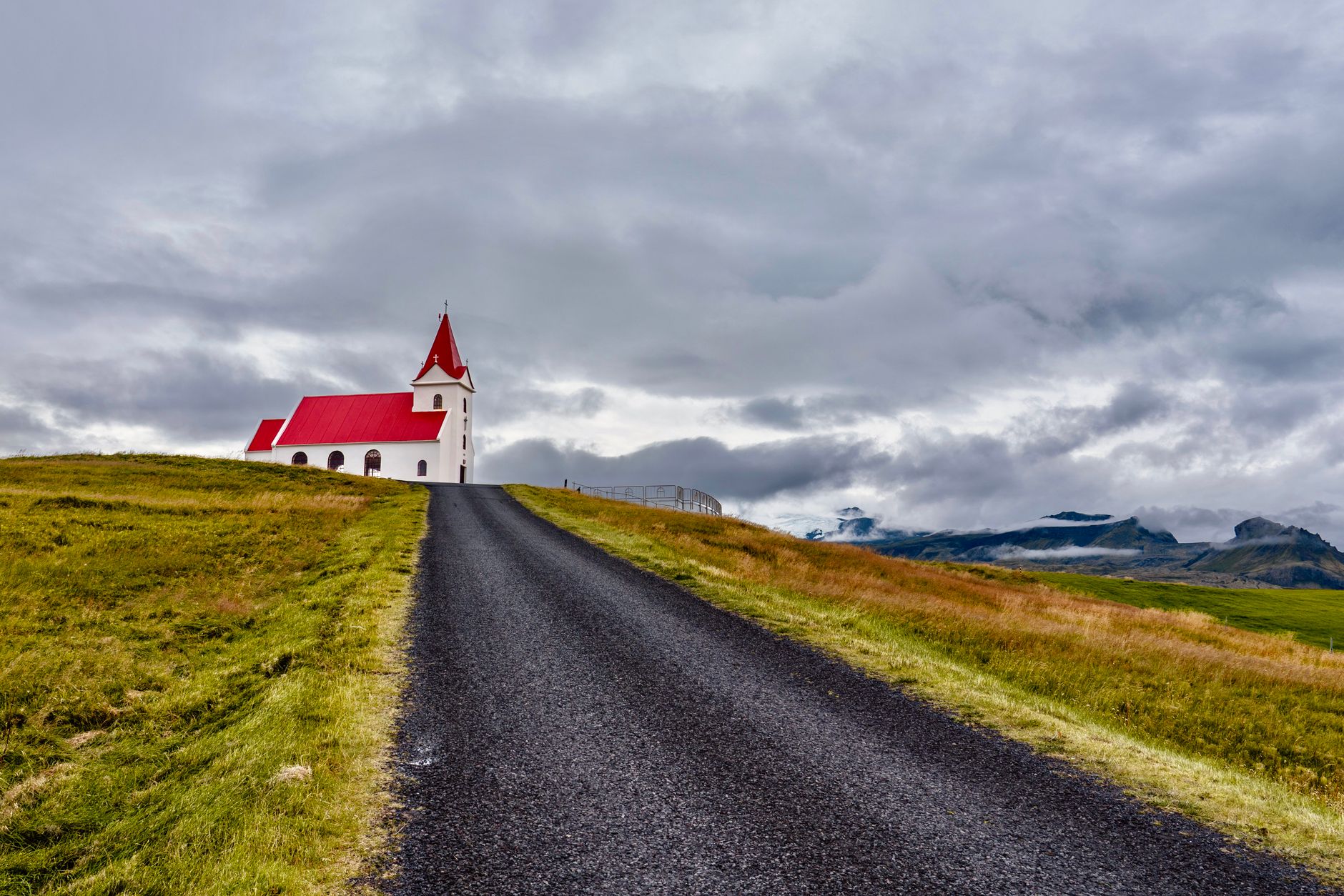 Breathtaking landscape with a red-roofed church on a hill in Iceland, under dramatic skies.