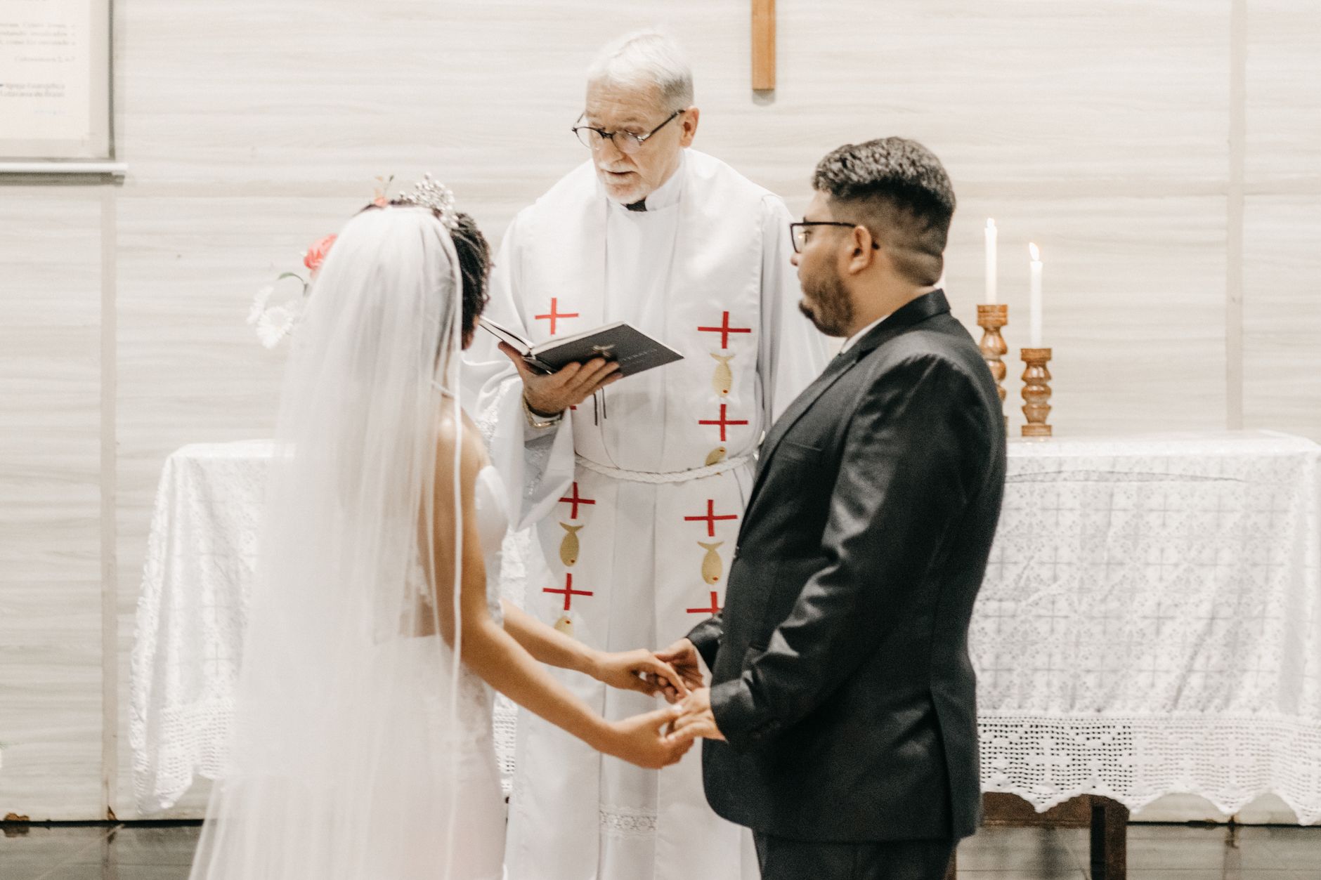 Newlyweds hold hands during a church ceremony led by a priest.