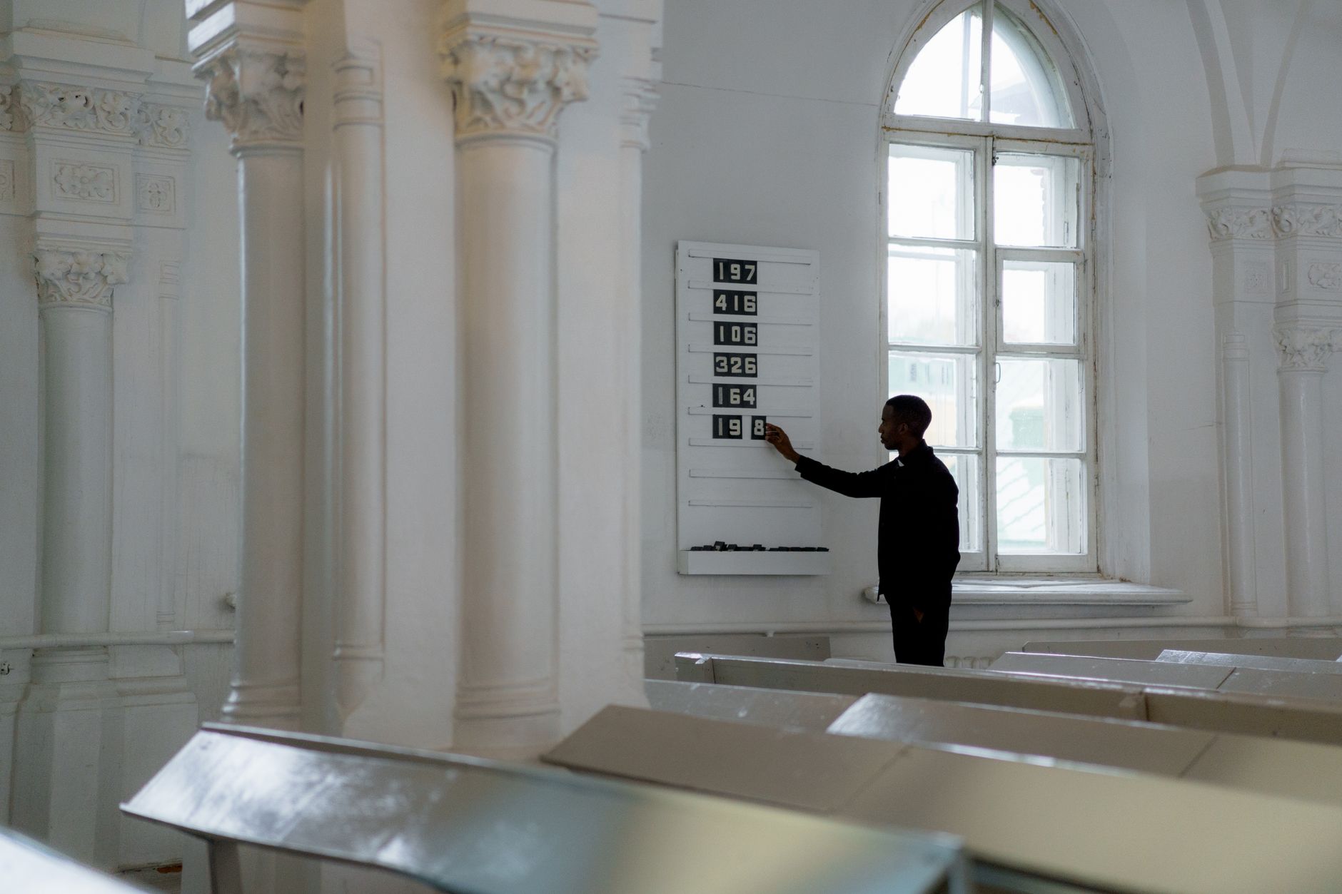 A man adjusts the hymn board numbers inside a historic church.
