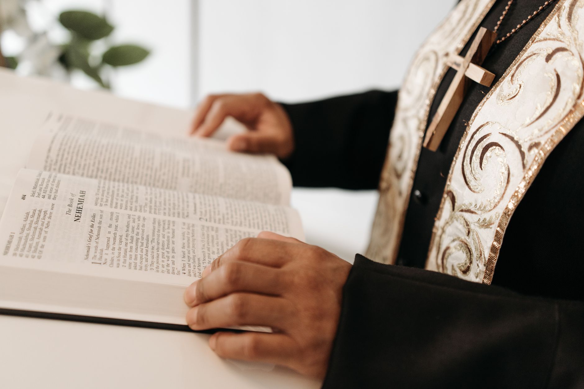 A pastor reads an open Bible, wearing religious attire with a cross necklace.
