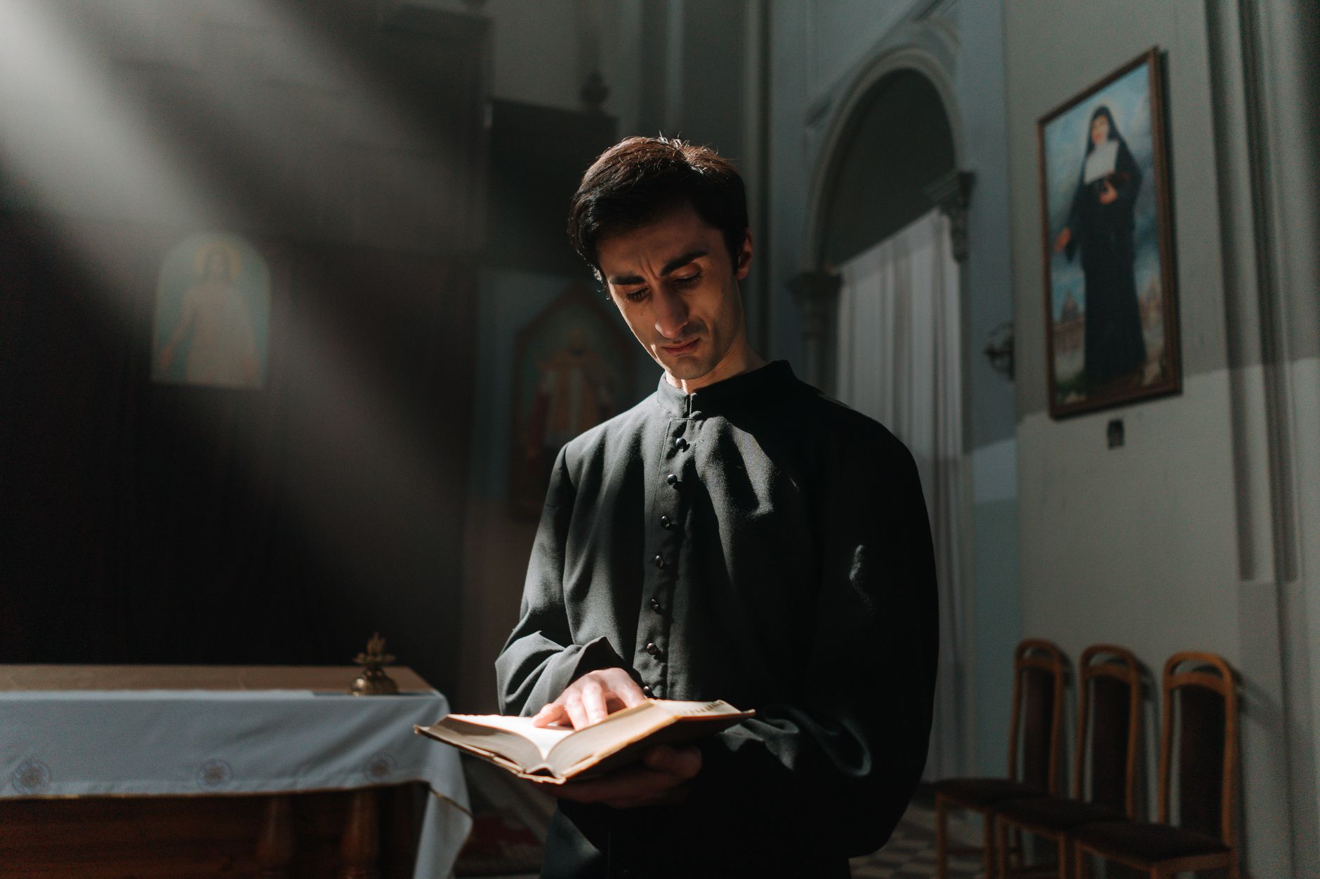 A priest reading a holy book in a church, illuminated by soft light.