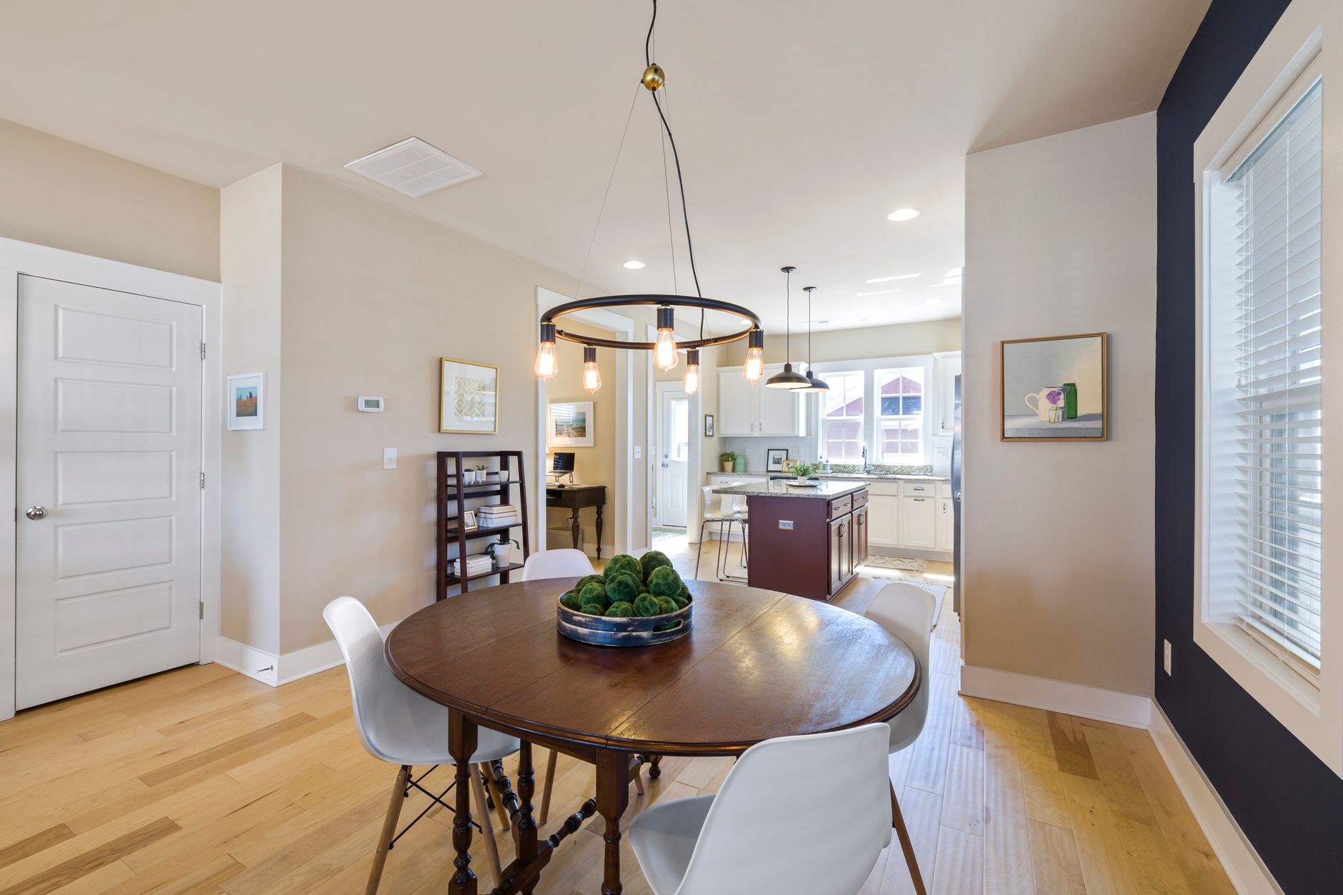 Spacious modern dining area with wooden table, white chairs, and kitchen view.