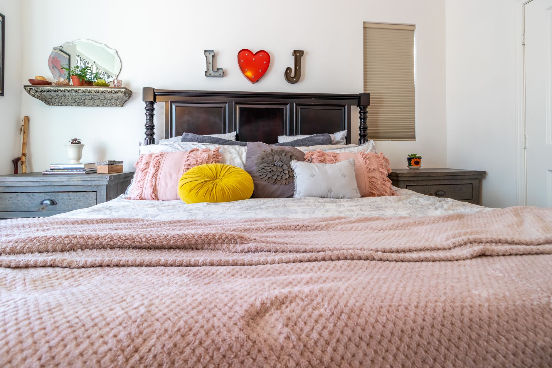 Interior of light bedroom with retro fashioned bed with soft pillows and blanket placed near wall decorated with mirror and decorative lamps in shape heart and letters