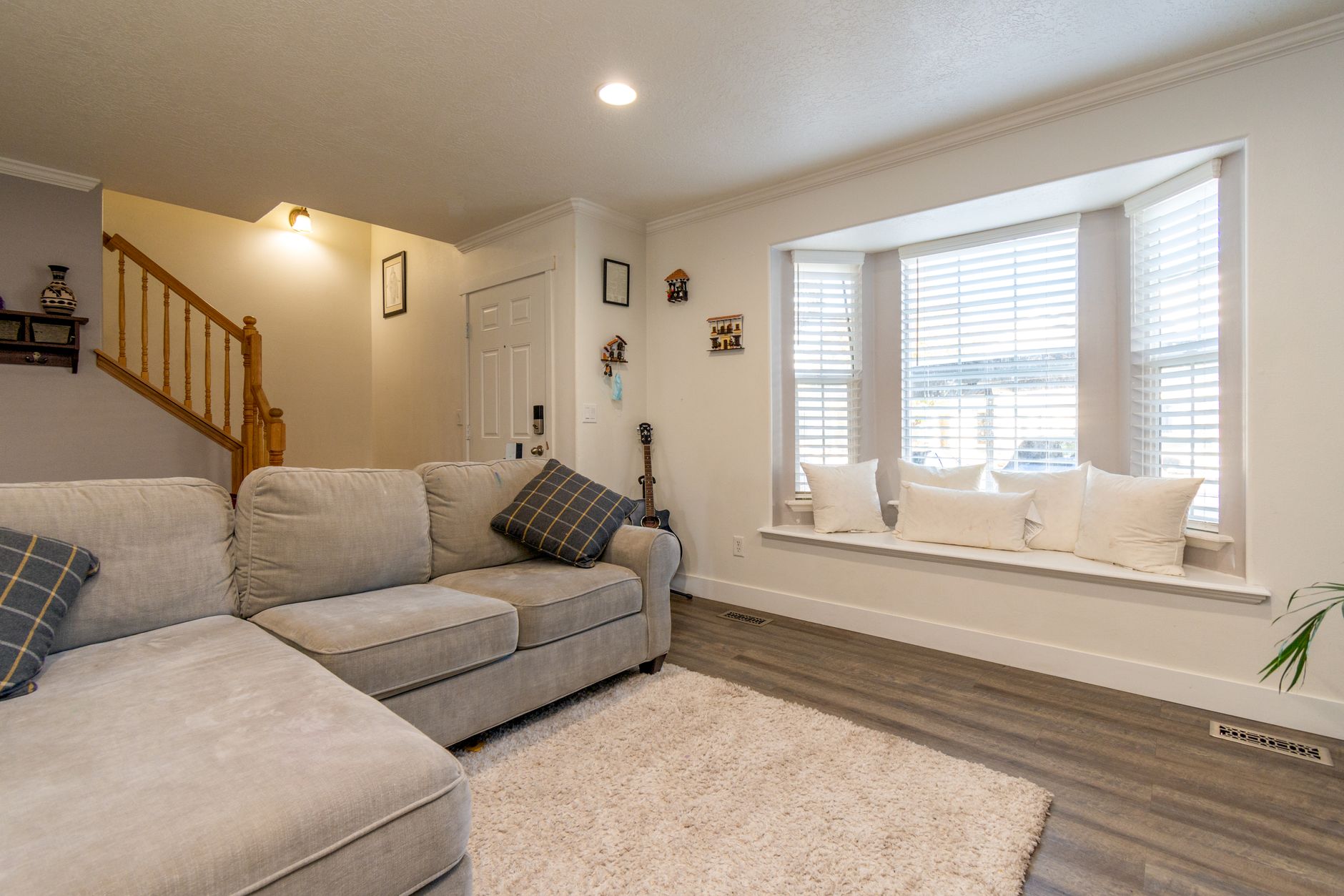 Bright and inviting living room featuring a beige sofa, large bay window, and wooden flooring.