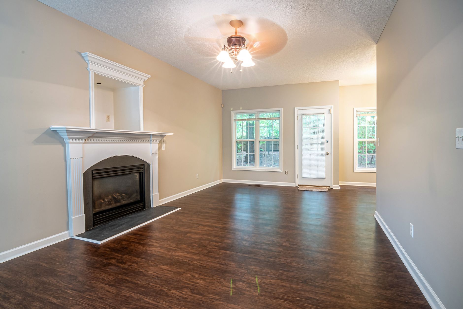Spacious and bright living room with hardwood floors, fireplace, and ceiling fan.