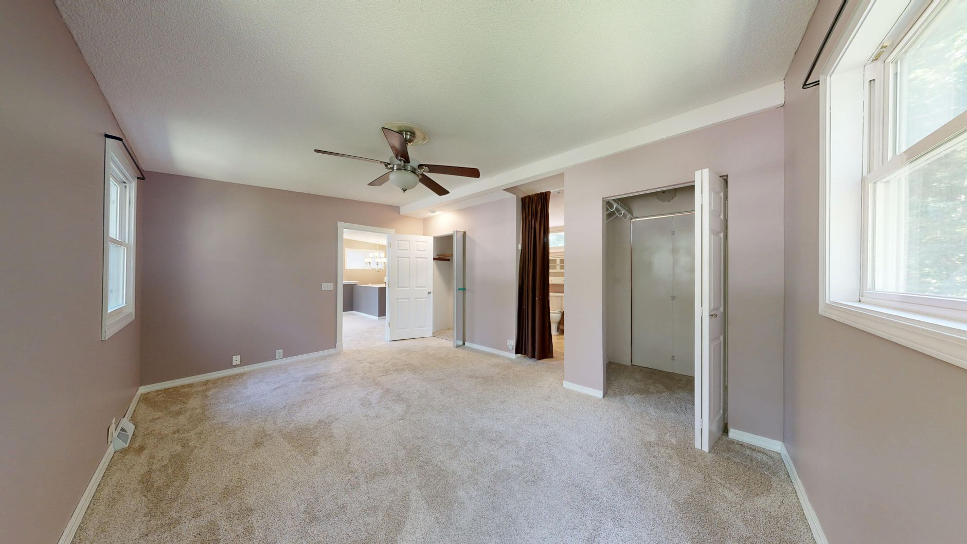 Spacious empty bedroom with neutral decor and natural light from multiple windows.
