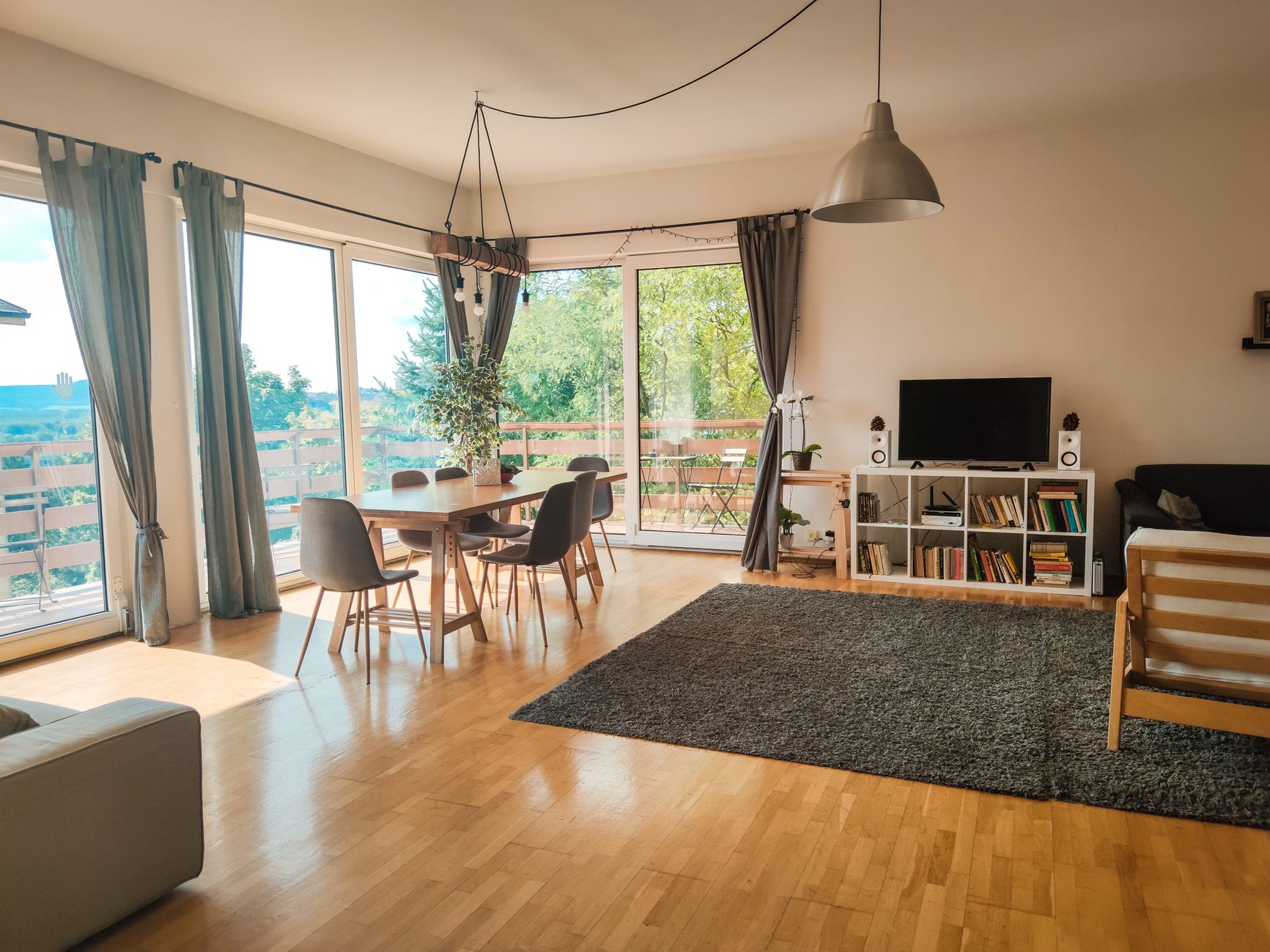 Spacious and inviting living room with wooden floor, dining area, and glass doors offering a scenic view.