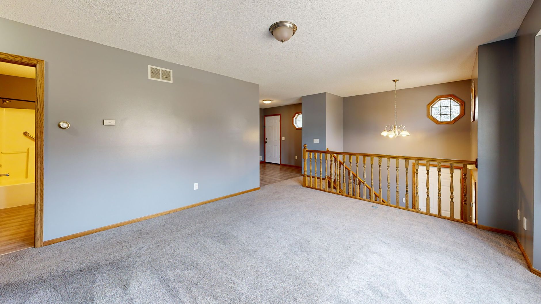 A bright, empty living room with carpet, wood accents, and natural light.