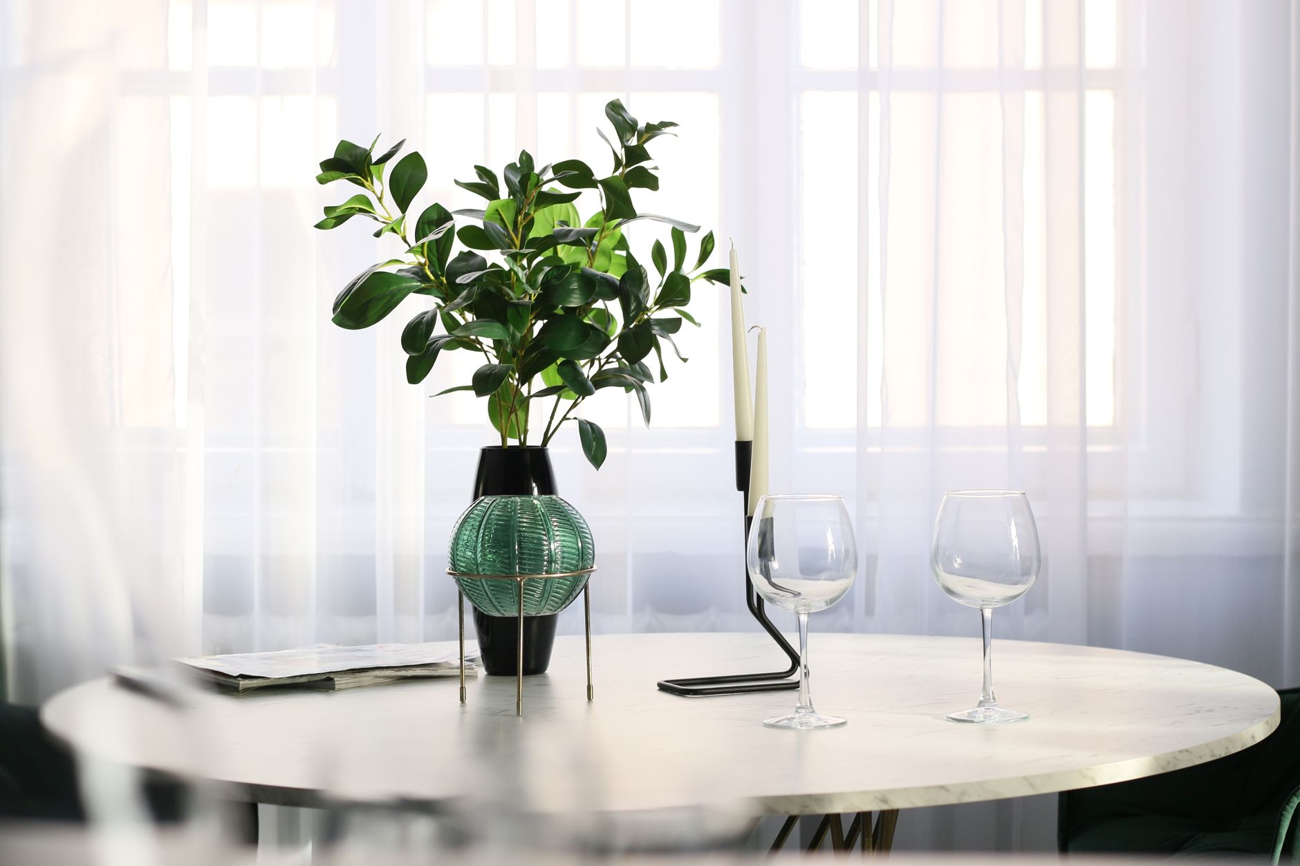 Elegant minimalist dining room with a plant and glassware on a table, bright and serene.