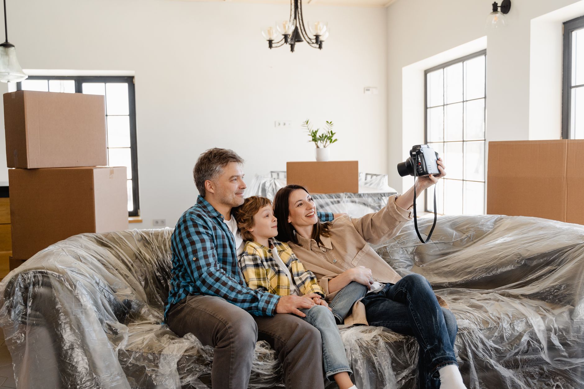 A happy family taking a selfie on their first day in a new home amidst unpacked boxes.