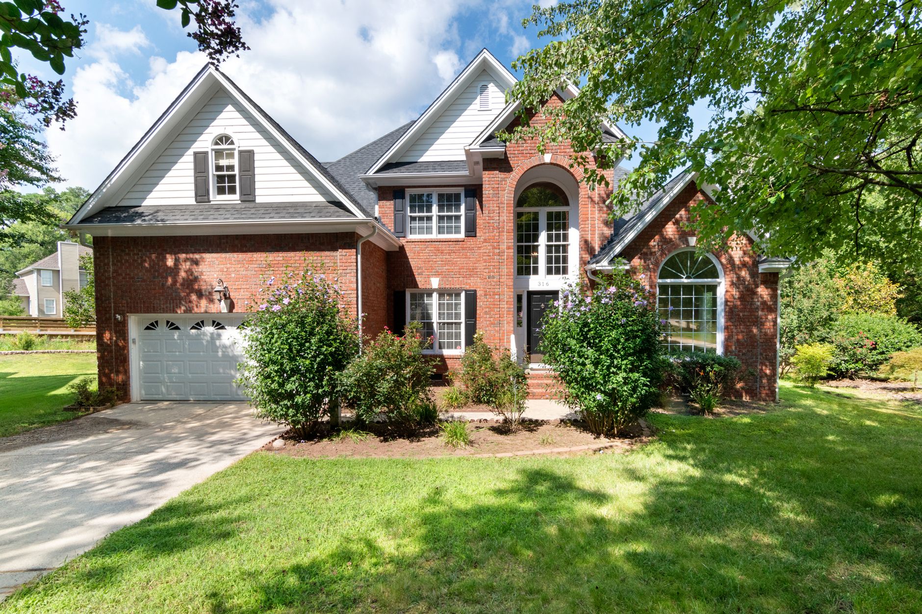 Charming two-story brick house in sunny suburb with lush front lawn.