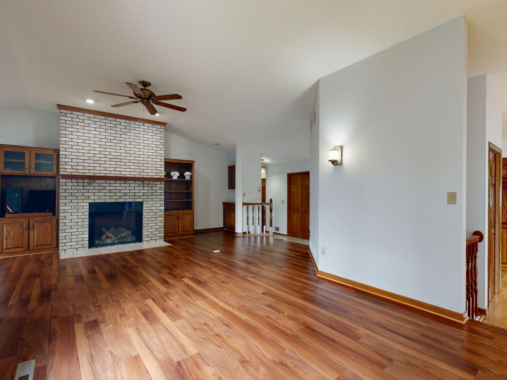 Bright and spacious living room featuring a brick fireplace, hardwood floors, and built-in cabinets.