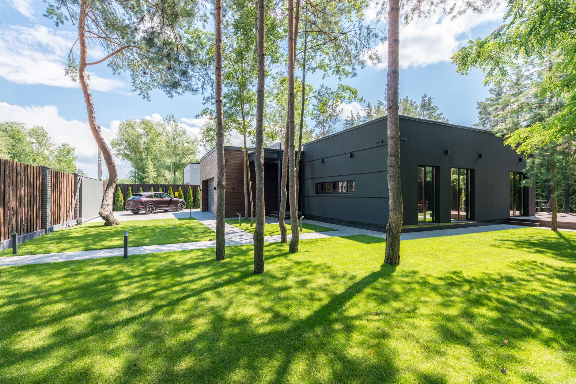 Contemporary house surrounded by lush green yard and trees, on a sunny day.