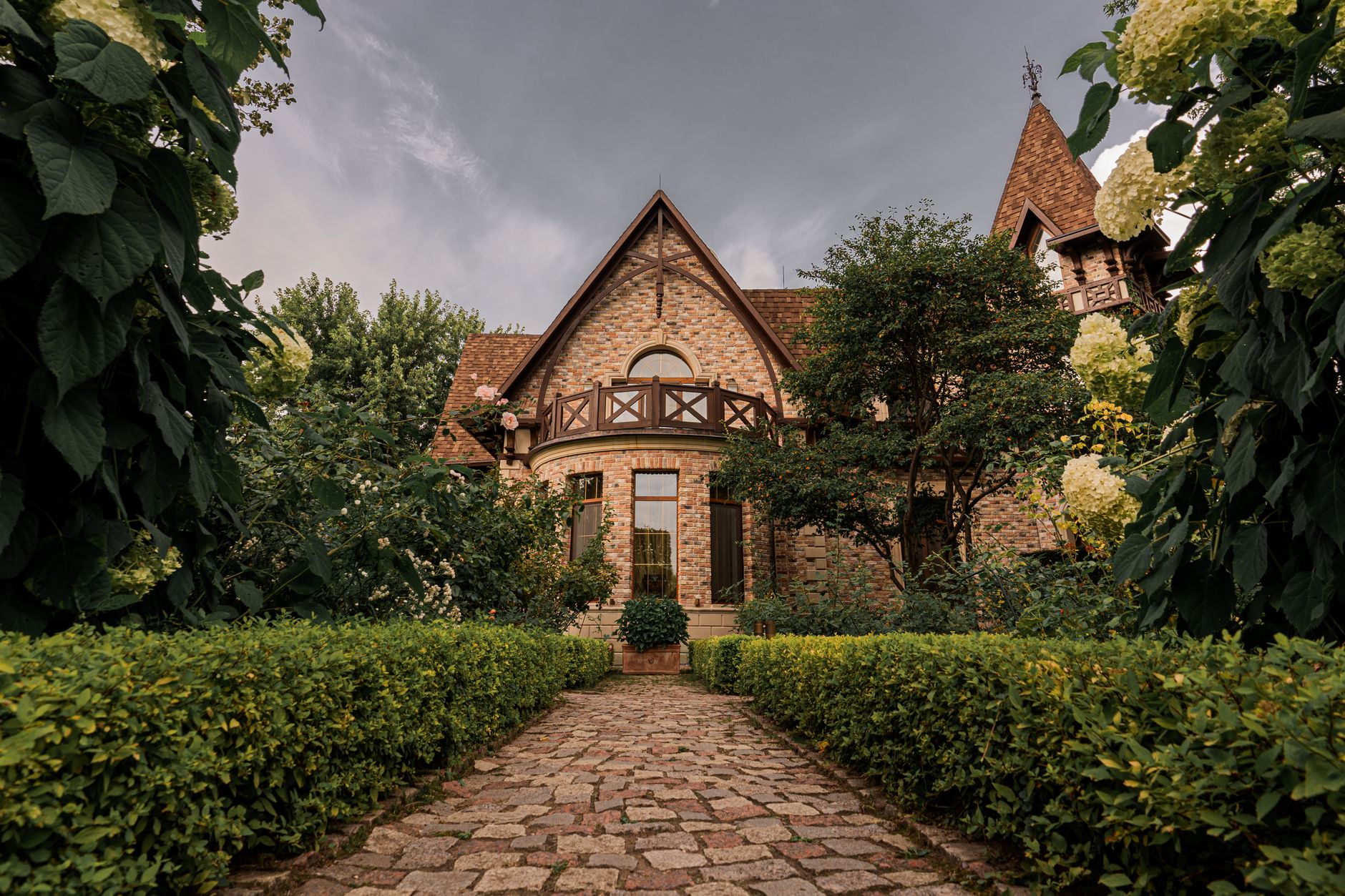 A picturesque brick house with landscaped garden and cobblestone path under a dramatic sky.