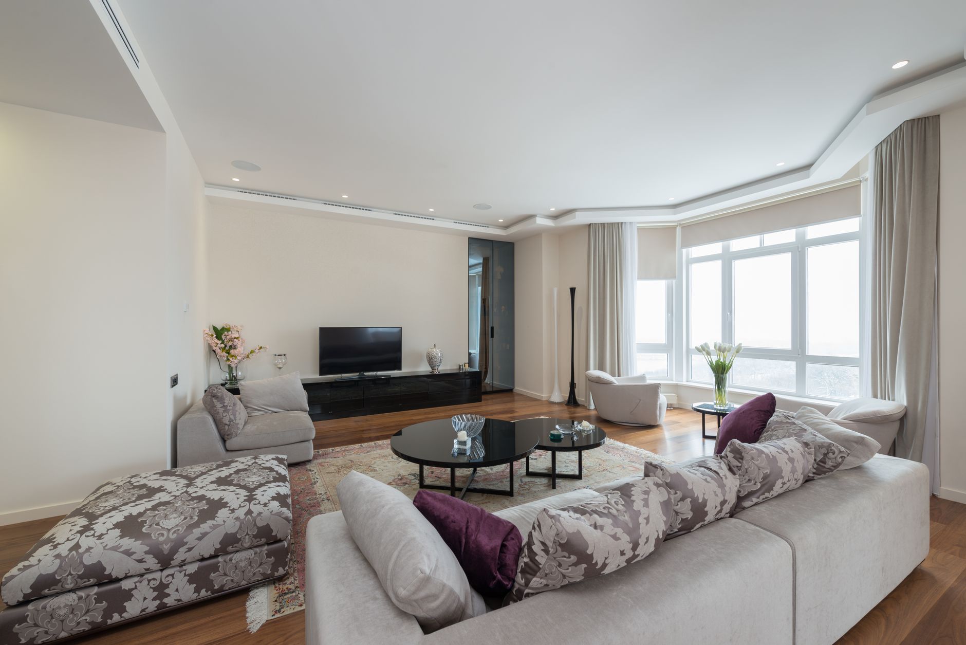 Cozy sofas and armchairs with soft cushions placed in front of round coffee tables in spacious elegant living room with modern TV and big windows