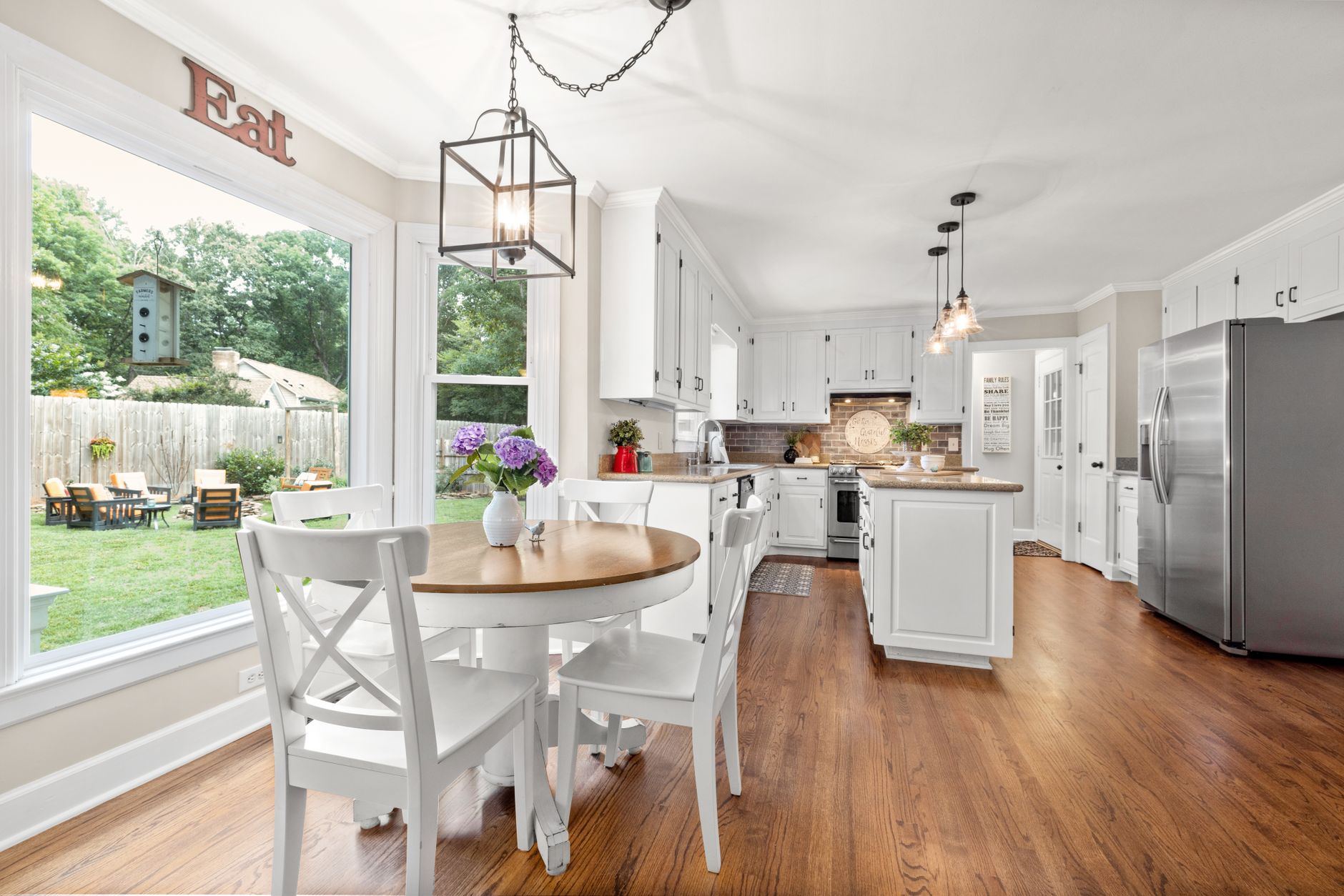 Modern kitchen with white cabinets and dining area with outdoor view.