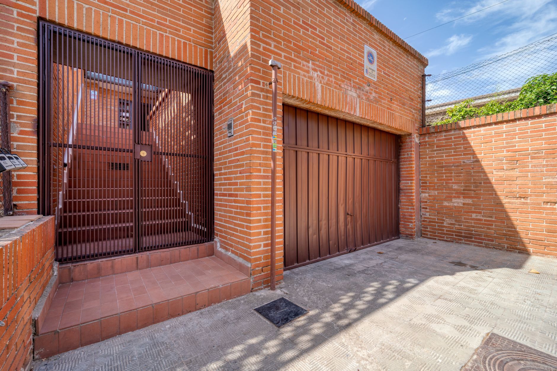 Modern brick facade featuring a metal gate and staircase, photographed in daylight for urban architectural design.