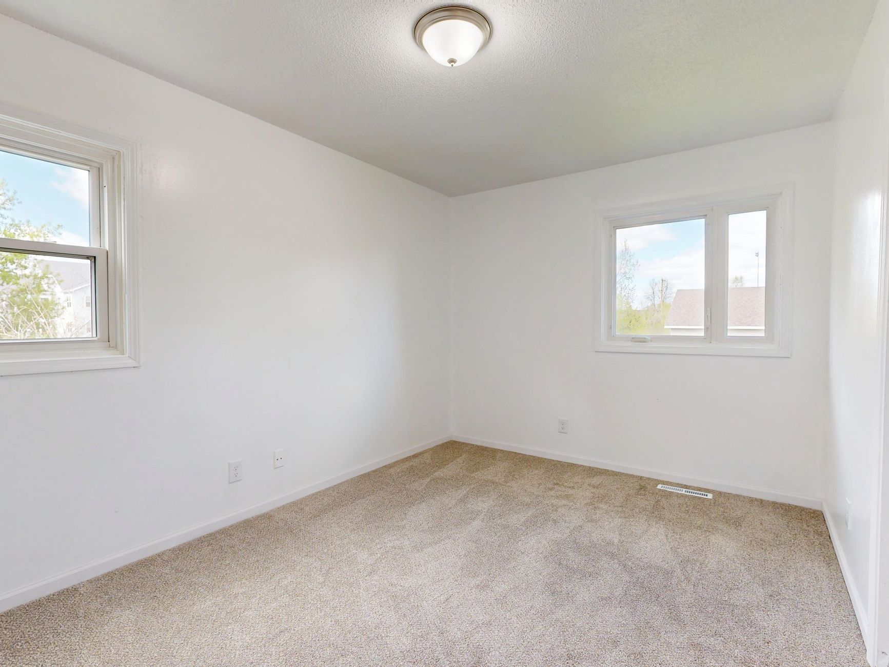 Spacious empty room with two windows, white walls, and neutral carpet flooring, ideal for real estate listings.
