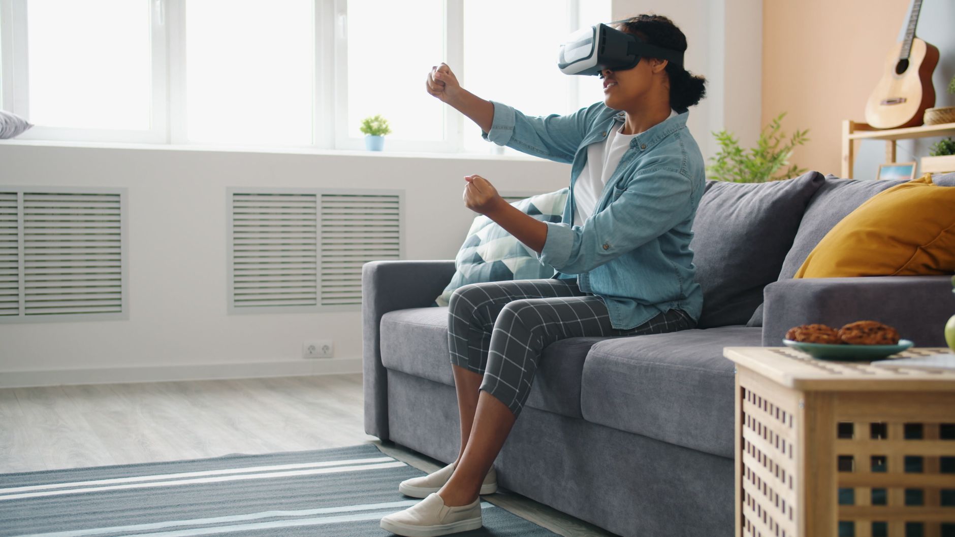 Woman sitting on sofa using VR headset, exploring virtual world with enthusiasm.