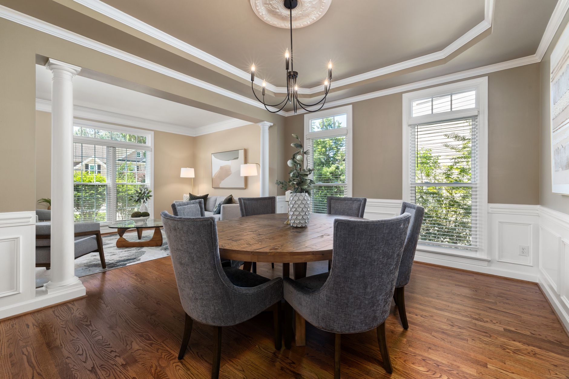 Spacious dining room featuring a round wooden table, modern chandelier, and comfortable gray chairs.