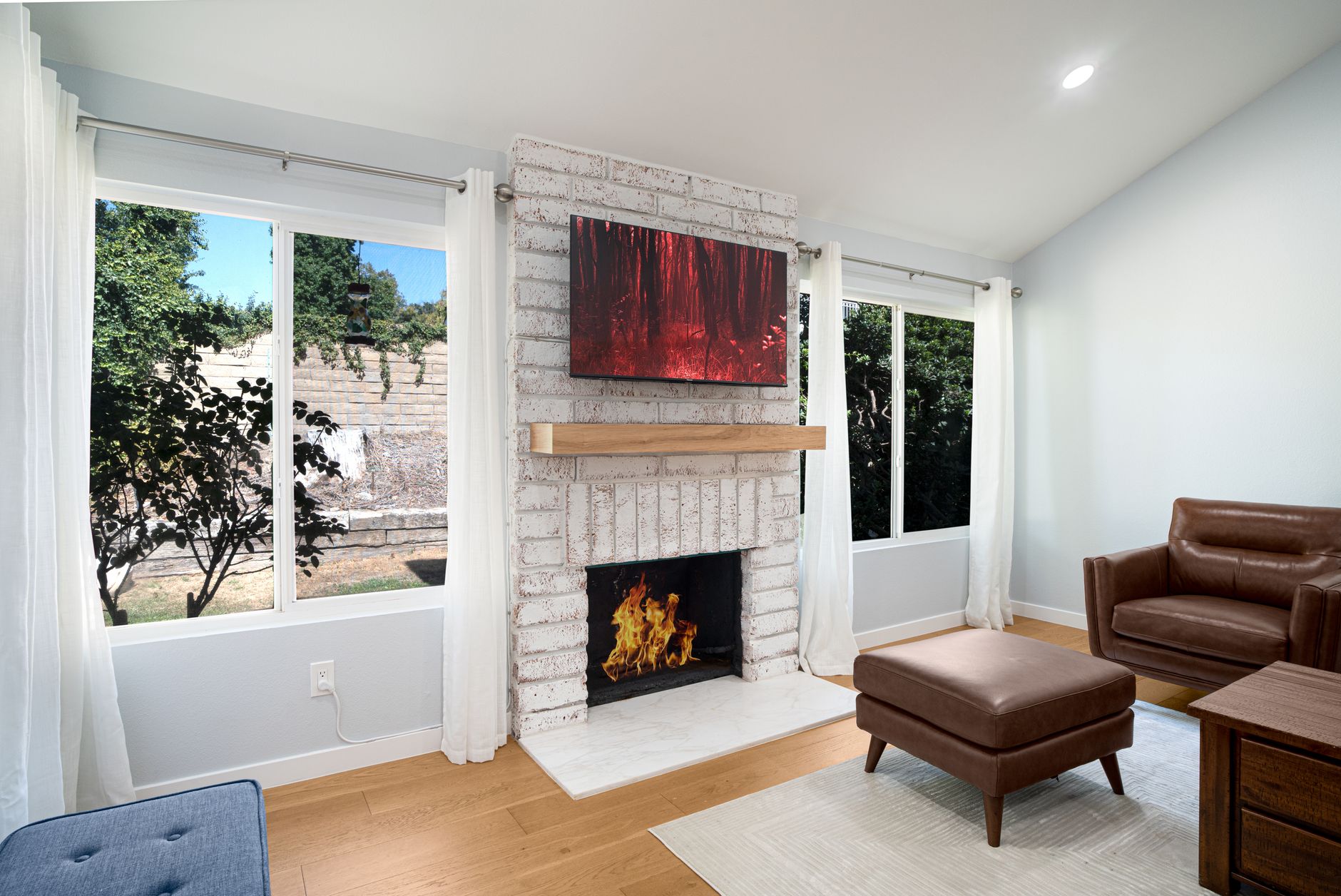 Contemporary living room with fireplace, leather chair, and nature view.