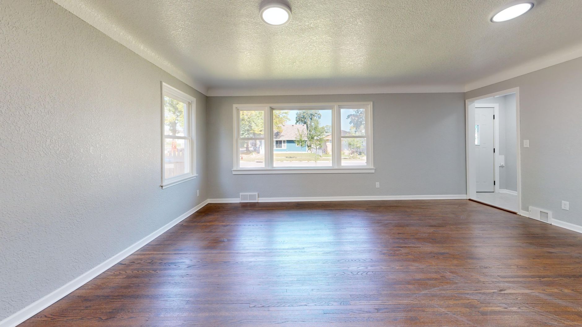 Bright empty room with hardwood floors and large windows, ideal for real estate.