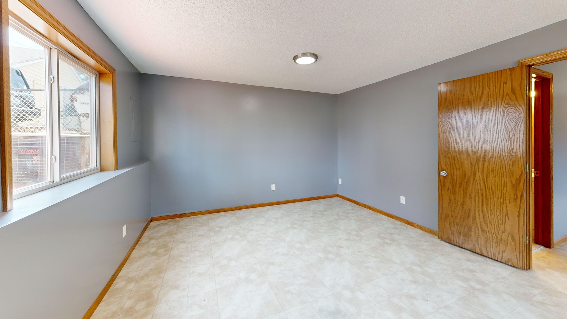 Spacious empty room with natural light from window and wooden door.