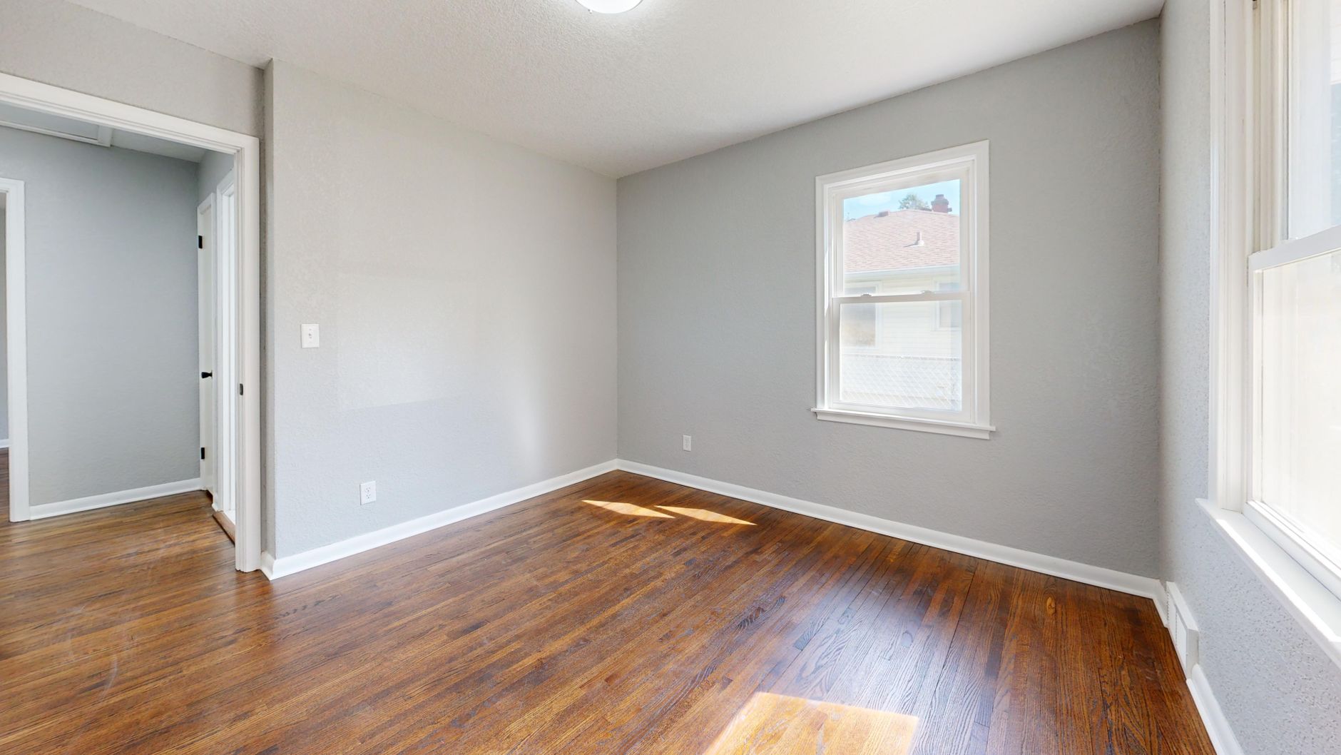 A bright empty room with wooden flooring and large windows, ready to furnish.