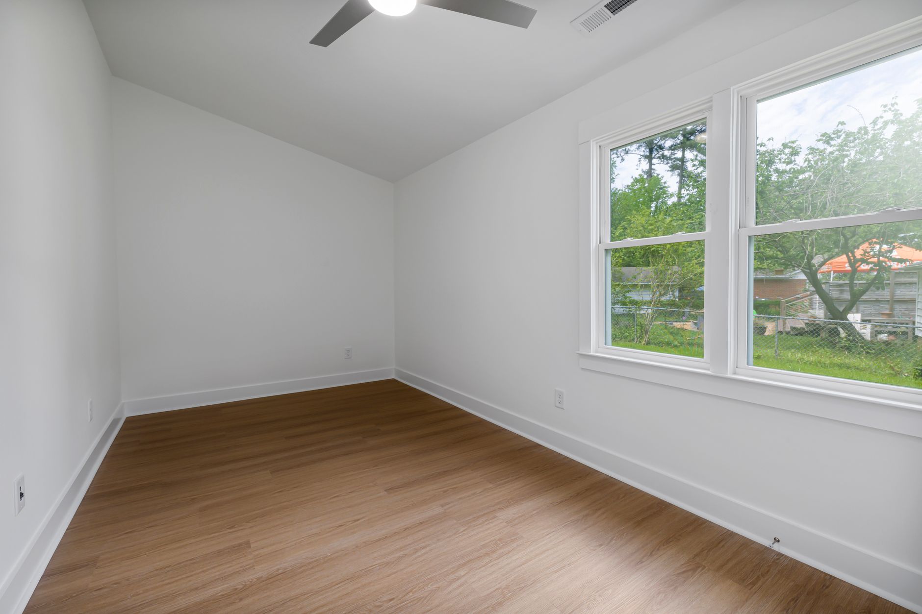 Spacious and bright minimalist room with light hardwood flooring and a ceiling fan.