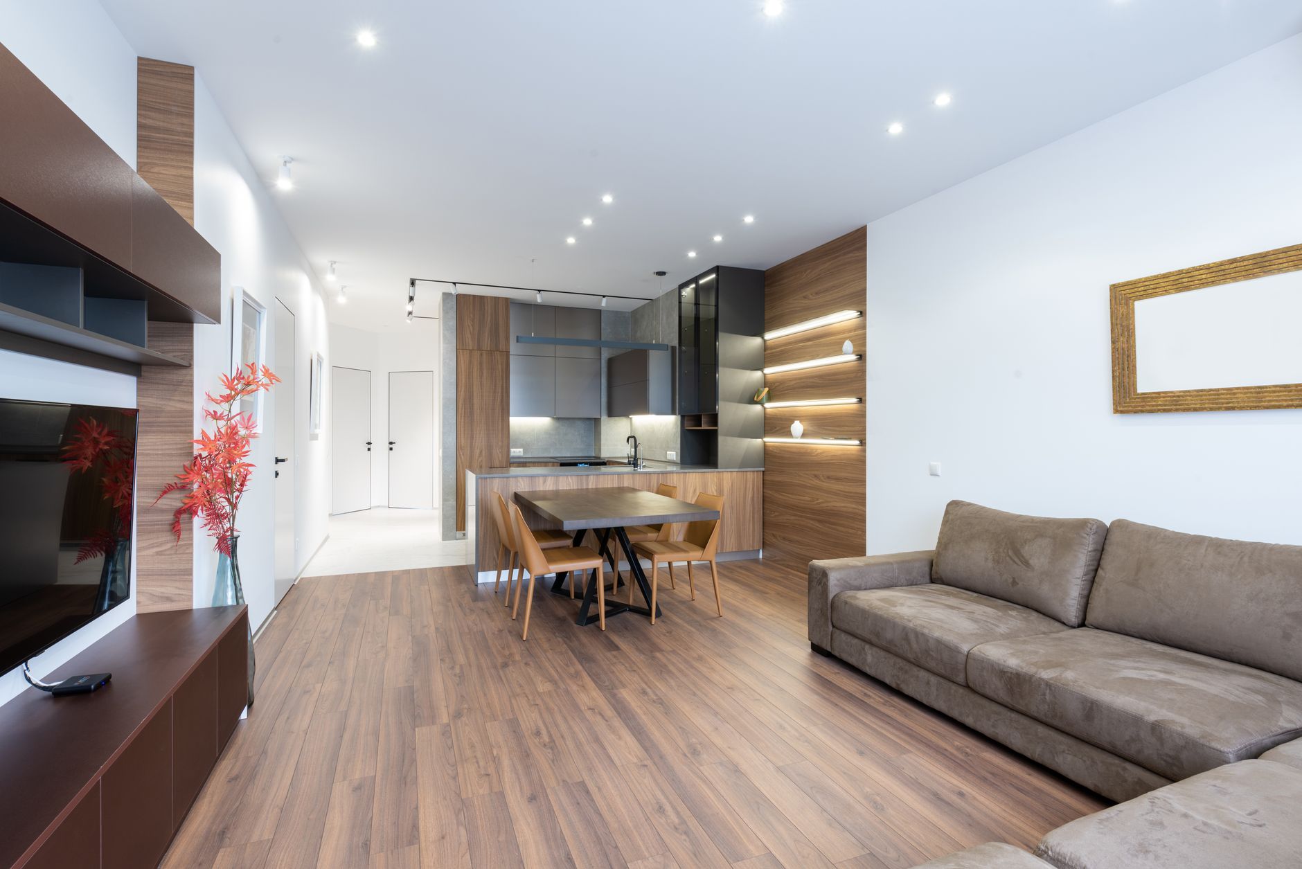 Interior of contemporary light decorated apartment with TV set placed against couch in modern apartment with table and kitchen counter