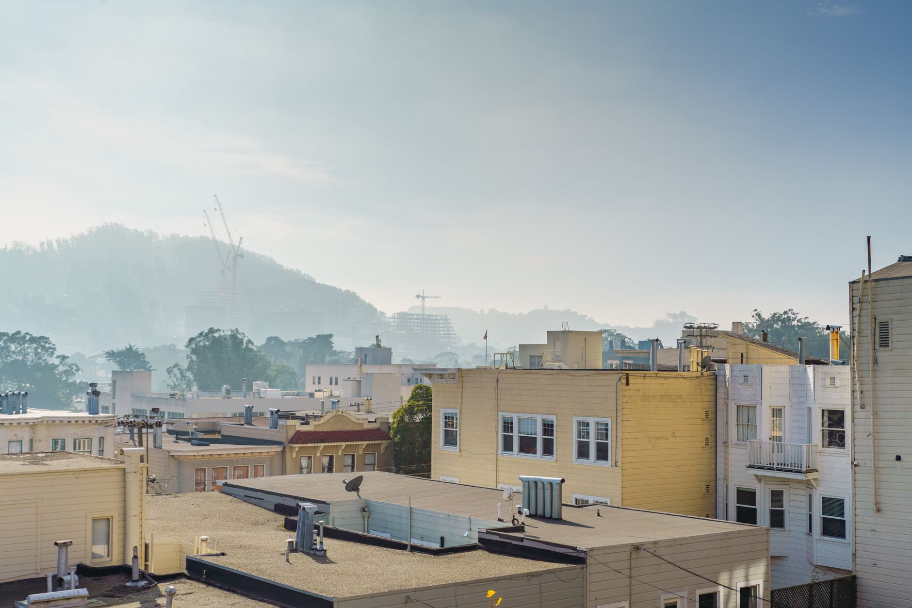A scenic rooftop view of urban buildings and distant hills on a sunny day.